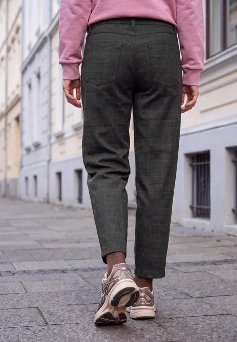 Mid Waist Barrel Leg Hose im Loose Fit inked grey Eine Person in karierter Hose, rosa Pulli und Sneakers geht auf einem Gehweg an Häusern vorbei.