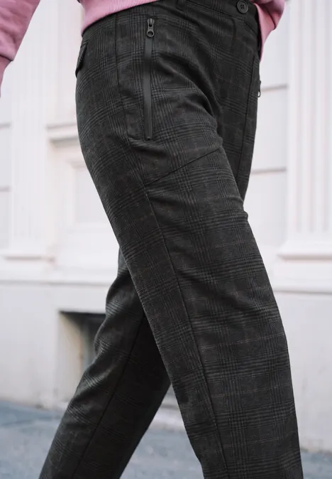 Mid Waist Barrel Leg Hose im Loose Fit inked grey Eine Detailaufnahme einer Person in dunkelgrauen, karierten Stoffhosen vor einem hellen Gebäude.