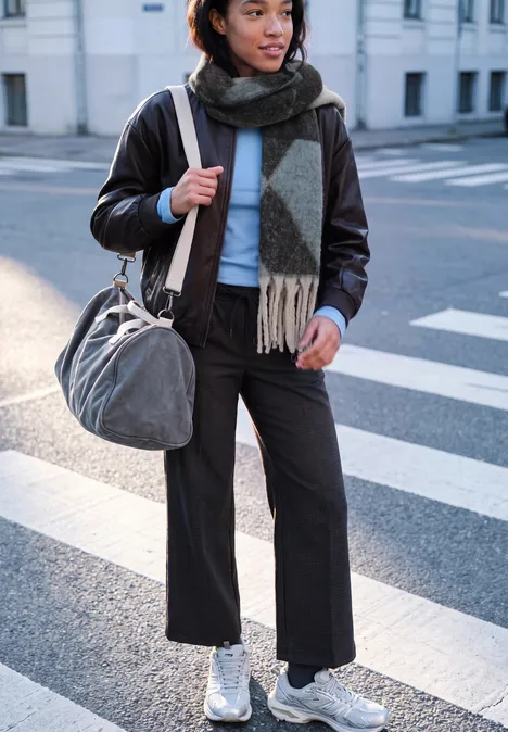 Lange sjaal met argylepatroon loom blue Frau in Lederjacke mit Schal und Tasche überquert Straße in weißen Sneakers.