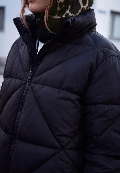 Eine Person trägt eine schwarze, gesteppte Daunenjacke mit hohem Kragen und Leopardenmuster-Stirnband.