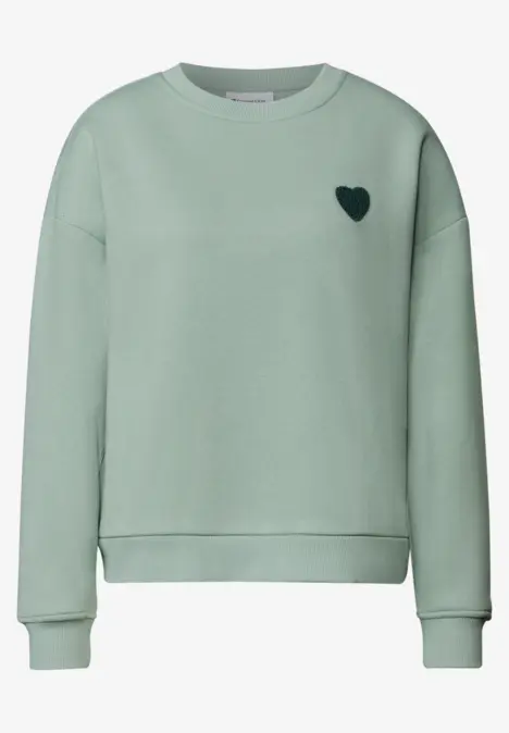 Un sweat vert menthe avec un petit cœur noir sur la poitrine.