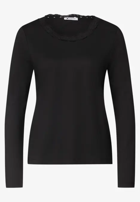 Schwarzes Langarmshirt mit Rüschen- und Spitzenbesatz am Rundhalsausschnitt.