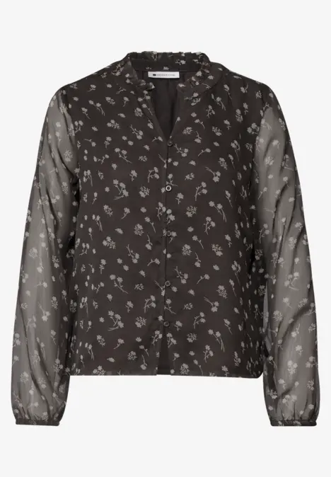 Zwarte blouse met knoopsluiting, klein wit bloemenprint en lange, transparante mouwen.