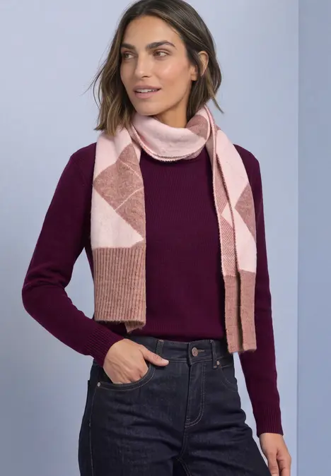 Vrouw in bordeauxrode trui, donkere jeans en roze sjaal met geometrisch motief.