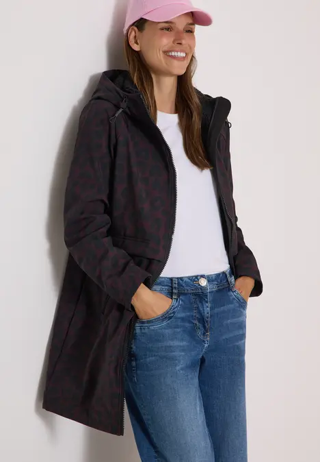 Femme en jean, T-shirt blanc et long manteau à capuche à motif, portant une casquette rose.