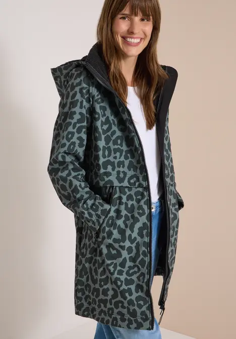 Femme souriante portant un manteau vert à capuche avec imprimé léopard noir.