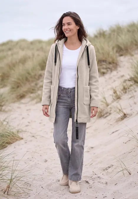 Femme en veste claire, t-shirt blanc et jean, se promenant sur des dunes sablonneuses aux herbes folles.