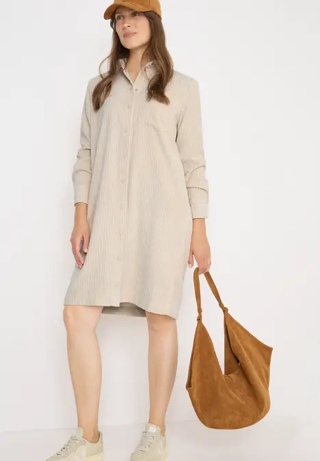 Frau in beigem Hemdkleid, brauner Kappe und Tasche, sportliche Schuhe.