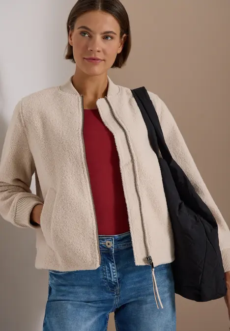 Frau in beiger Jacke, rotem Top, Jeans und schwarzer Tasche.
