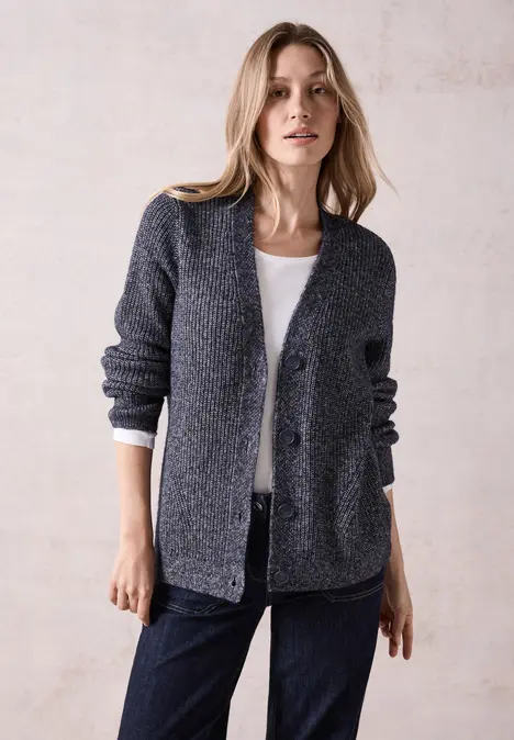 Frau trägt graue Strickjacke, weißes Shirt und Jeans.