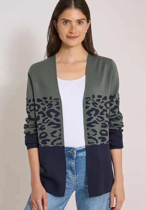 Dame trägt salbeigrünen Strickcardigan mit Leopardenmuster, kombiniert mit weißem Top und blauer Jeans.