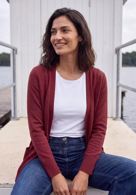 Frau steht entspannt auf einem Steg, trägt roten Cardigan und Jeans.