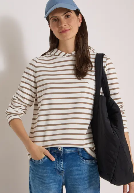 Frau in gestreiftem Pullover und Jeans mit lächelnder Ausstrahlung und schwarzer Tasche über der Schulter.