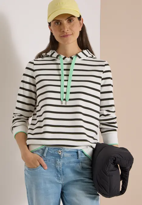 Frau in einem gestreiften Kapuzen-Sweatshirt mit grünen Details hält eine Steppjacke.