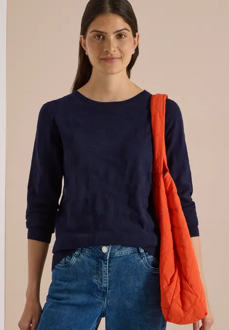 Eine junge Frau mit dunkelblauer Bluse und Jeans trägt eine orangefarbene Umhängetasche.