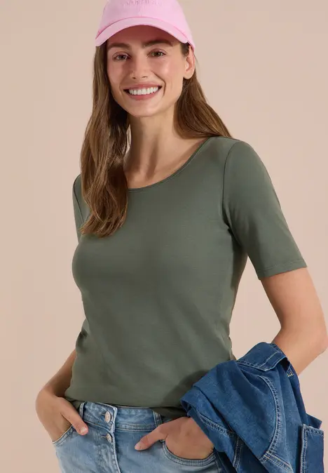 Frau mit grünem T-Shirt, Jeans und Jeansjacke in der Hand, rosa Cap