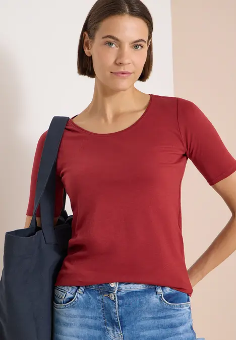 Frau trägt rotes T-Shirt und blaue Tasche über der Schulter, sichtbar ab Brusthöhe.