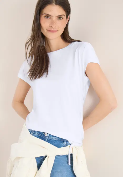 Kobieta w białym T-shircie i niebieskich dżinsach, z kurtką przewiązaną w talii.