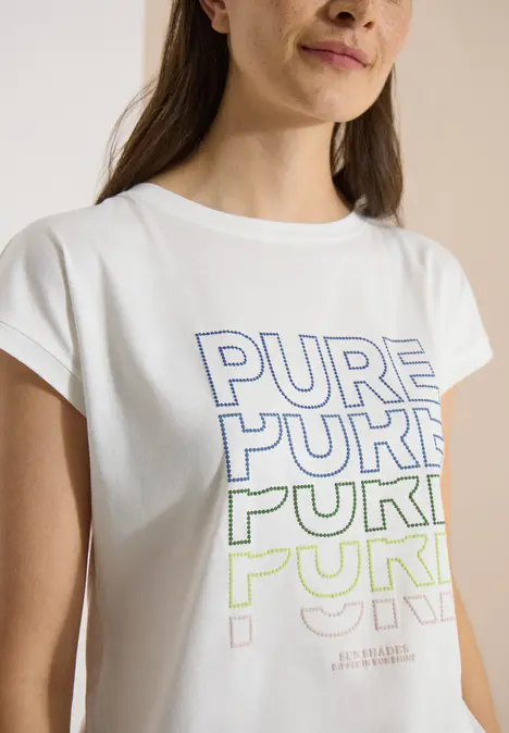 Frau trägt weißes T-Shirt mit dem Wort 'PURE' in Blau und Grün mehrfach bedruckt.