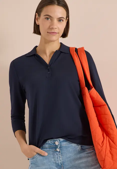 Person mit dunkelblauem Langarm-Poloshirt und orangefarbener gesteppter Umhängetasche.