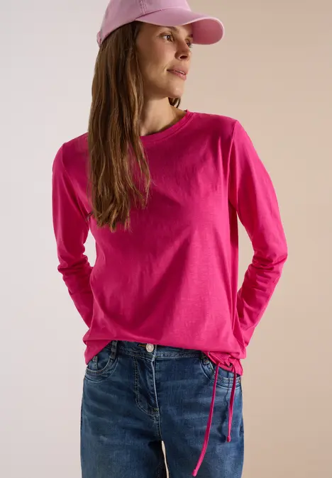 Frau trägt pinkes Langarmshirt mit Tunnelzug, Jeans und pinkes Cap.