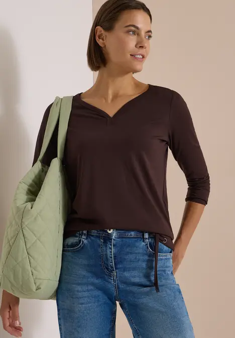 Frau mit dunklem V-Ausschnitt-Oberteil, blauen Jeans und gesteppten, hellgrünen Shopper über der Schulter.