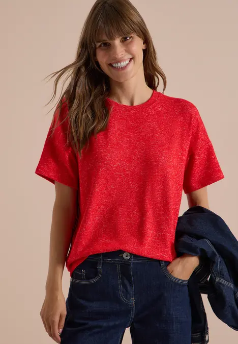 Lachende vrouw in rood T-shirt en spijkerbroek met spijkerjasje in hand.