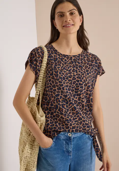 Frau trägt Leo-Shirt, Jeans und hält eine geflochtene Tasche.