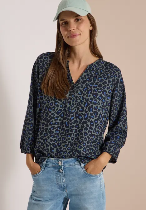 Frau trägt blaue, gemusterte Bluse, Jeans und weiße Kappe