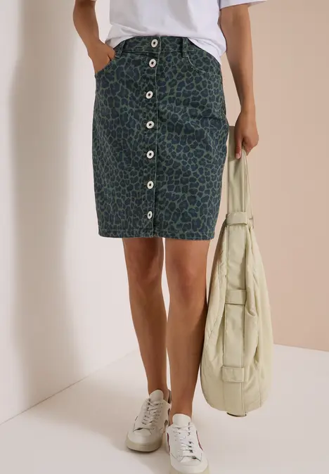 Frau trägt Midirock mit vorderer Knopfleiste, weiße Sneaker und beige Tragetasche.