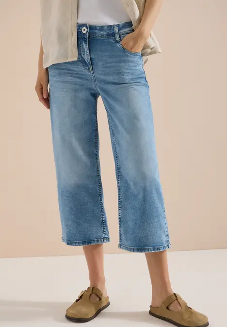 Frau trägt hellblaue, weite Cropped-Jeans und braune Clogs.