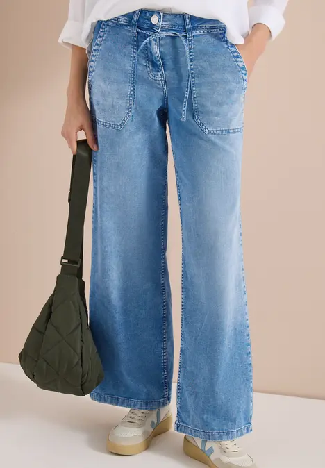 Helle, weite Denim-Jeans mit Tunnelzugbund und Eingriffstaschen, kombiniert mit Sneakers und einer schwarzen Tasche.