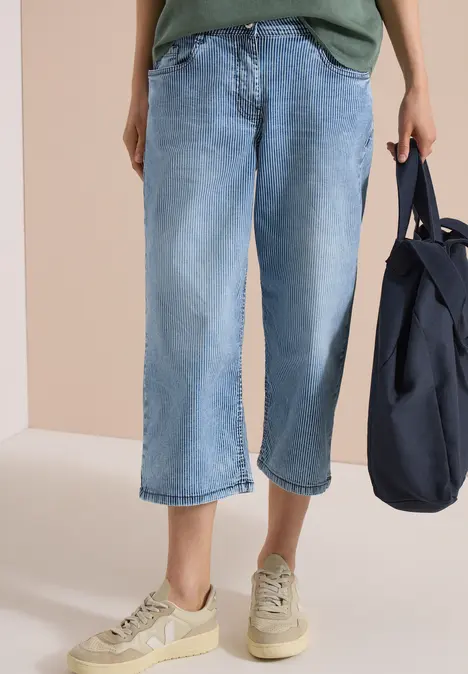 Person in weiten, hellblauen Jeans-Culottes, beigen Sneakern und dunkelblauer Tasche