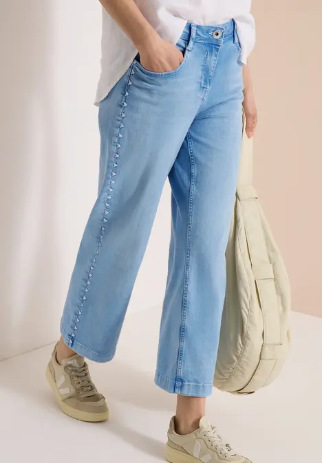 Helle, gerade geschnittene Jeans mit Zierknöpfen an den Seiten, kombiniert mit beigen Sneakers und Tasche.