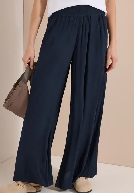 Weite dunkelblaue Damenhose kombiniert mit einer braunen Handtasche und beigen Schuhen.