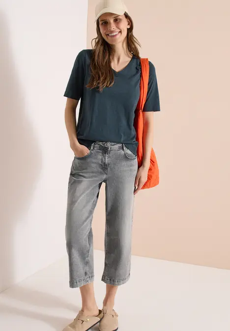 Frau in dunkelblauem T-Shirt, grauen Jeans und orangefarbener Umhängetasche.