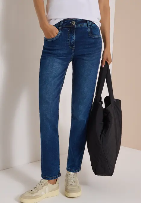 Person trägt blaue Straight-Leg-Jeans, weiße Sneaker und hält eine schwarze Tasche.