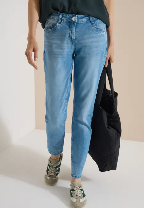 Unterkörper einer Person in hellblauen Jeans, Sneakern und schwarzer Tasche.