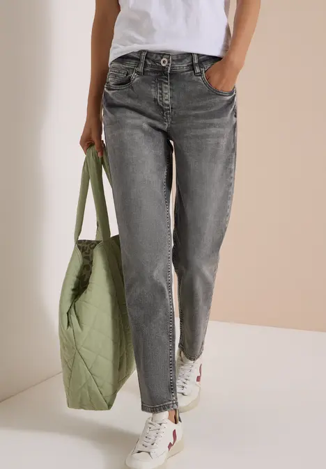 Person in grauen Jeans, weißem Shirt und weißen Sneakern trägt eine große grüne Stepp-Tasche.