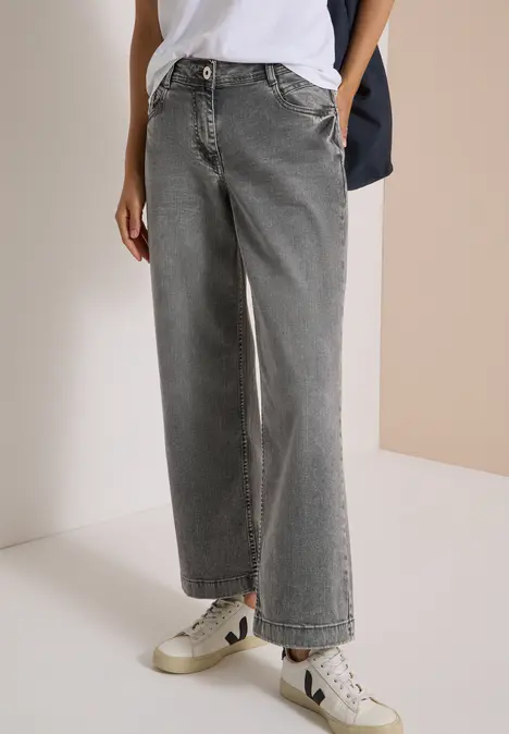 Ein Model trägt weite, graue High-Waist-Jeans und weiße Sneaker.