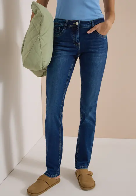 Person trägt blaue Jeans, hellblaues Top und braune Hausschuhe, hält eine hellgrüne Stepptasche.