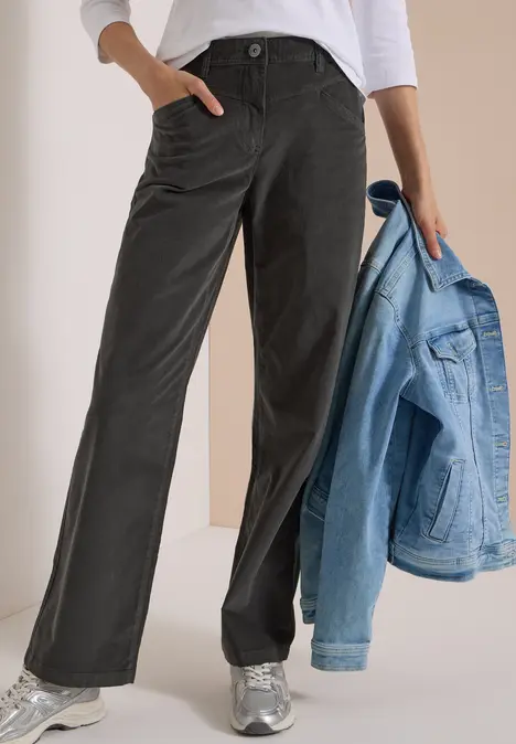 Person trägt schwarze, weite Hose mit Taschen, weiße Bluse und silberne Sneaker, hält eine hellblaue Jeansjacke.