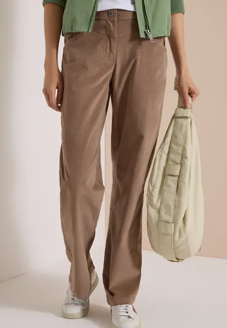 Person trägt braune Cordhose, weiße Sneaker und hält eine beigefarbene gesteppte Tasche.