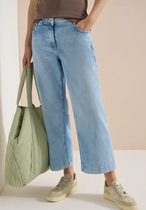 Frau trägt weite hellblaue Jeans, grüne Stepp-Tasche und beige Sneaker.