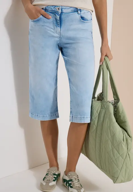 Damenlook mit Jeans-Bermudas, weißen Sneakern mit grünen Details und großer gesteppter grüner Tasche.