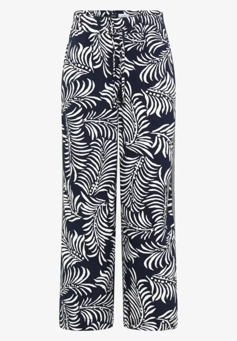 Pantalon ample à fond sombre et motif feuille tropicale blanc.