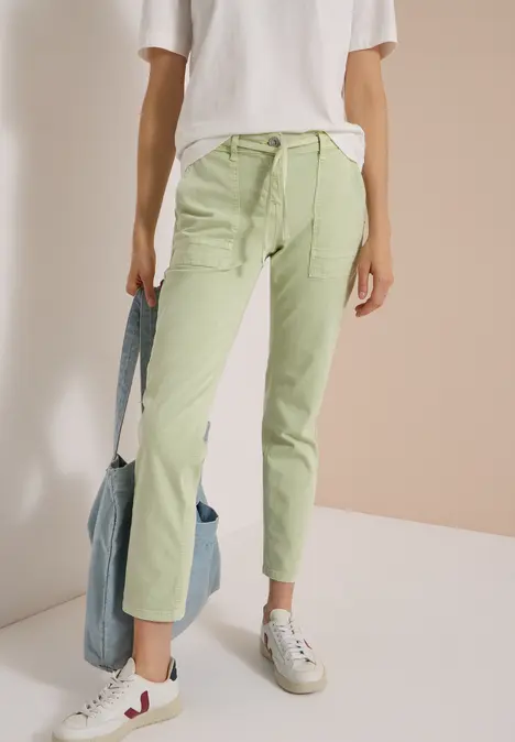 Eine Person trägt helle, grüne Hosen, weiße Sneakers und hält eine blaue Tasche.