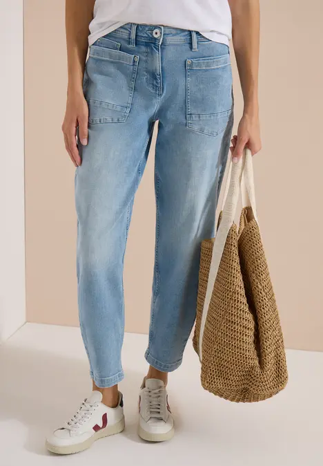Person trägt helle Jeans, weiße Sneaker und hält eine geflochtene Strohtasche.