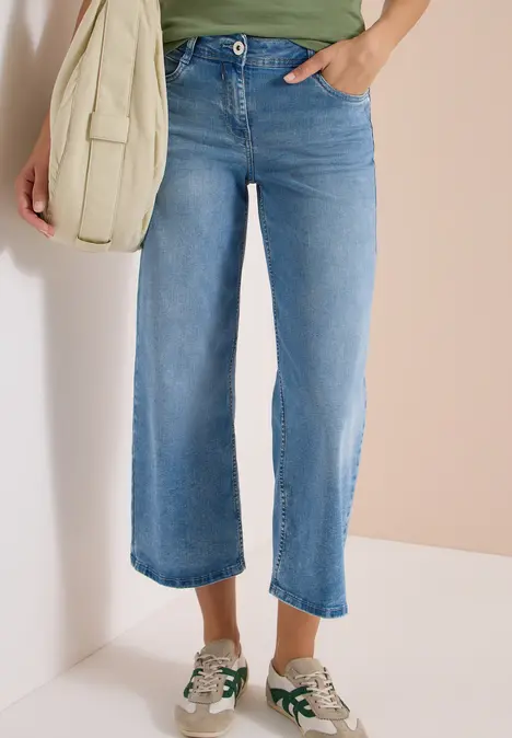 Helle Cropped-Jeans mit geradem Bein, weiße Sneaker und beige Umhängetasche.