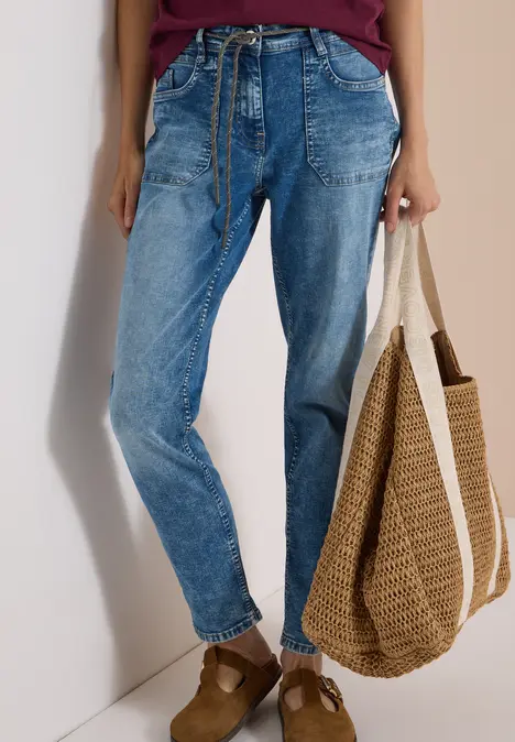 Frau trägt lässige blaue Baggy-Jeans und hält eine große Strohtasche.